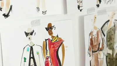 A close-up shot of several fashion design sketches taped to a white surface. In the foreground, two figures are prominently featured. The figure on the left wears a white jacket with dark lapels and sunglasses. The figure on the right is dressed in a red outfit with a yellow banana design on the shoulder and also wears sunglasses. Other partially visible sketches show more fashion figures in various poses and outfits. The style is illustrative with visible watercolor and pen strokes.