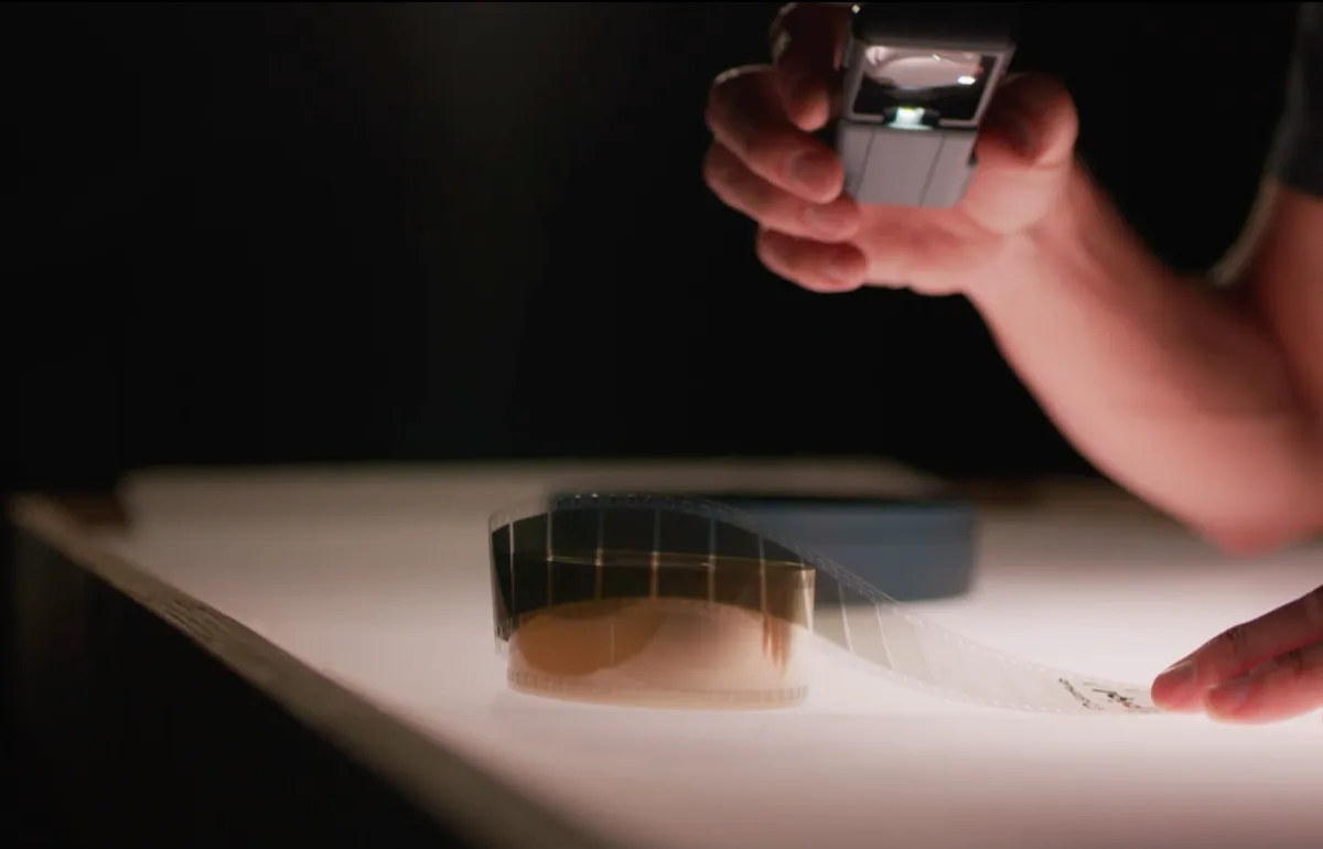 A hand holding a reel of piqlFilm above a light table.